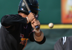 A photograph taken from behind a poised batter as a baseball appears to hang in mid-air in front of him