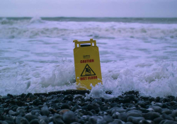 A "Caution: Wet Floor" sits on a beach and is enveloped by the tide