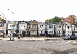 A panoramic shot of a urban street, mostly deserted with the exception of a small cluster of people near a streetlight
