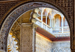 A photograph from inside of an archway that looks toward a balcony in the courtyard outside