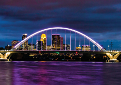 The skyline of Minnepolis seen through an arched bridge suspended over purple water