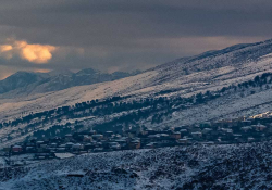 A photograph of a small village on a mountainside, shrouded in snow and shadow