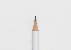 The tip of a white pencil laying on a piece of white paper